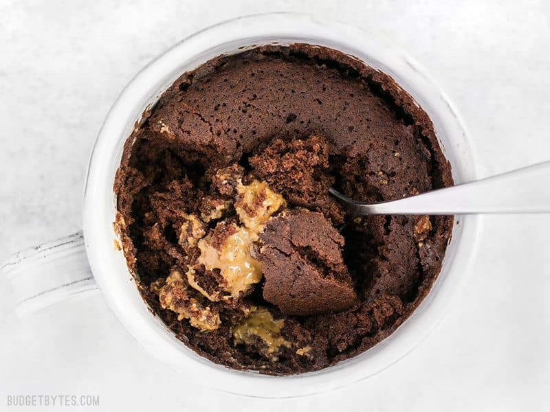 An overhead view of a spoon digging into a chocolate mug cake with peanut butter