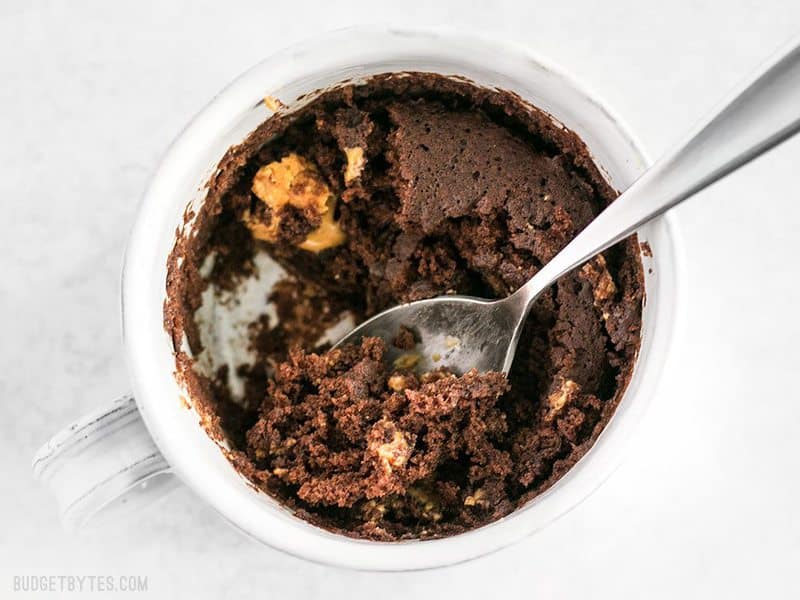 Half eaten chocolate mug cake viewed from above, with the spoon left in the mug.