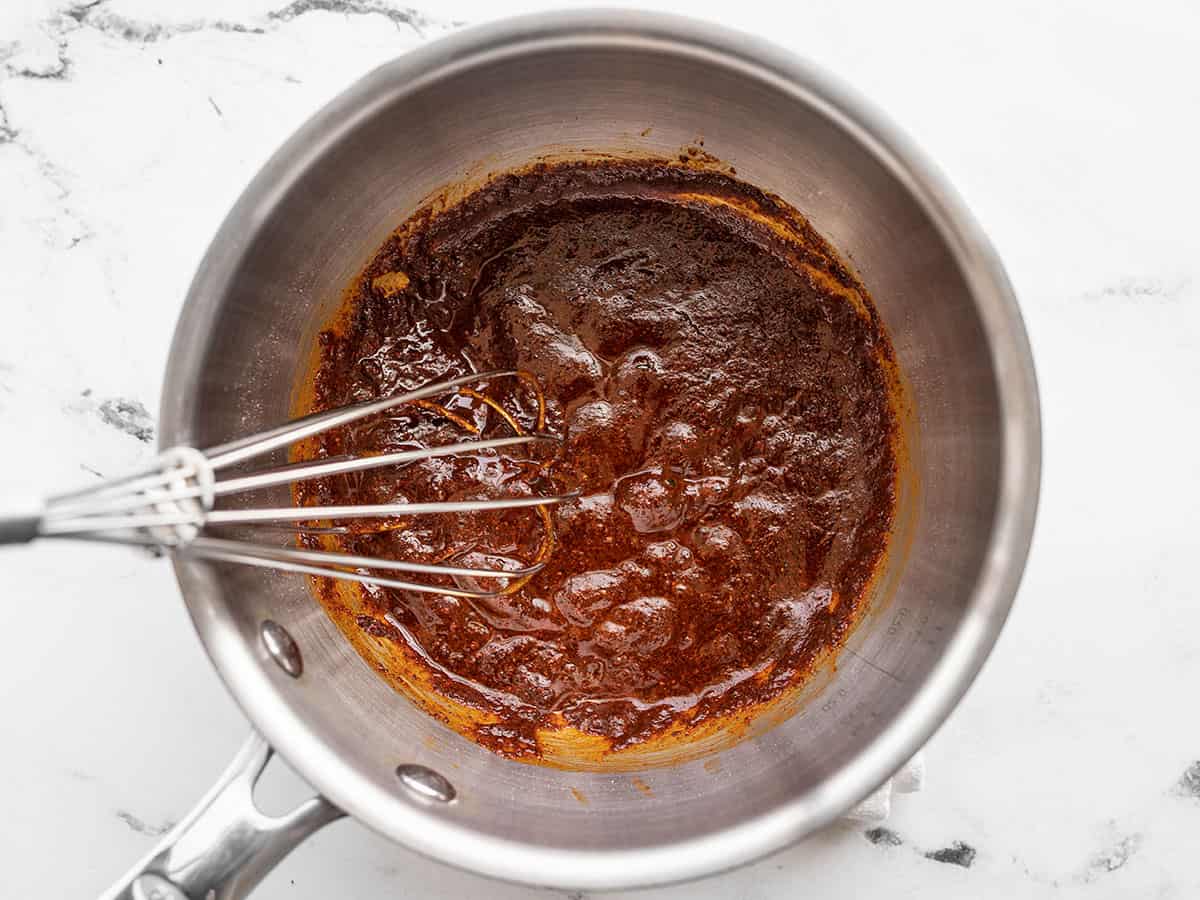boiling chili powder and roux in a sauce pot with a whisk.