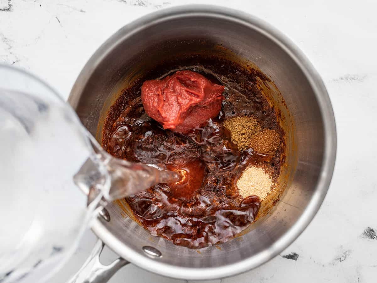 water being poured into the pot with tomato paste and spices.