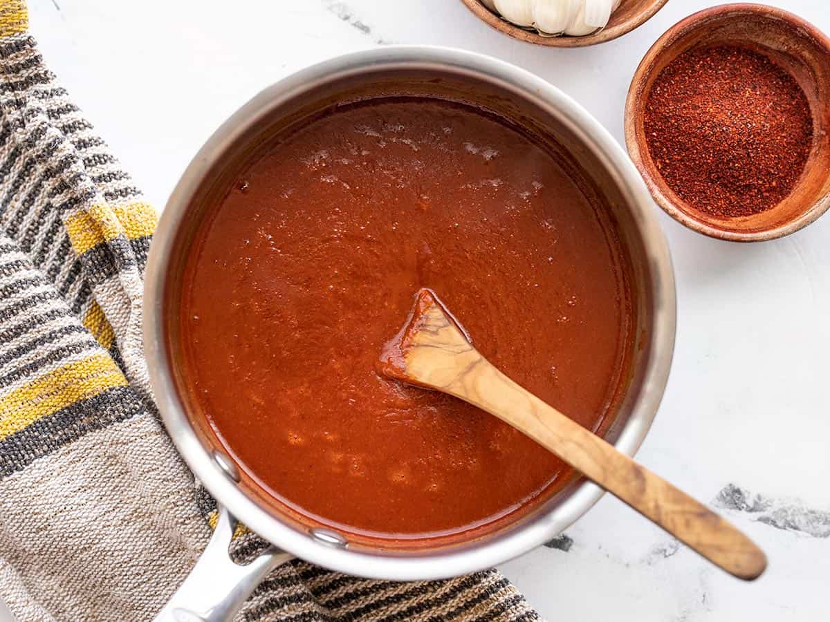 Enchilada sauce in a sauce pot with a wooden spoon.