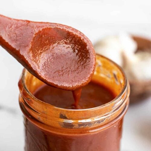 close up of enchilada sauce dripping off a wooden spoon into a jar.