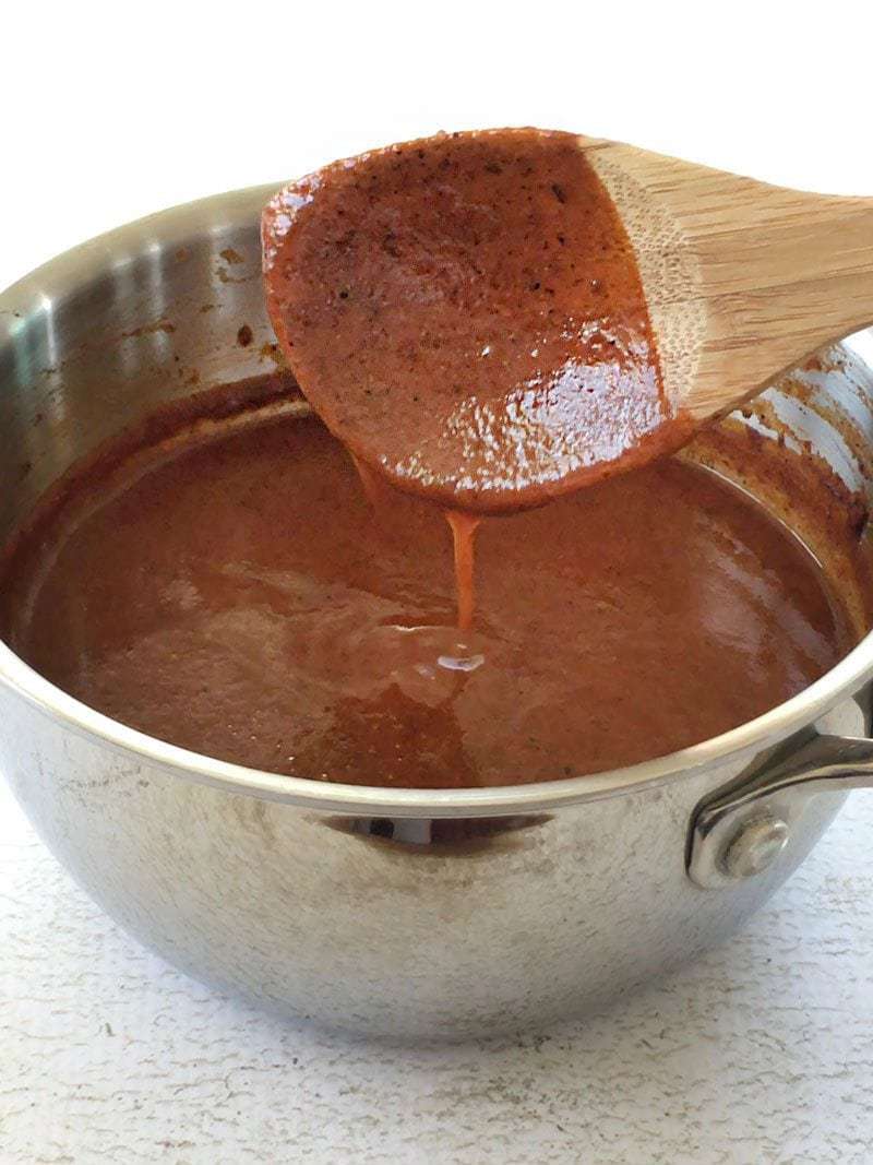 Thick Easy Red Enchilada Sauce dripping off of a spoon into the pot.