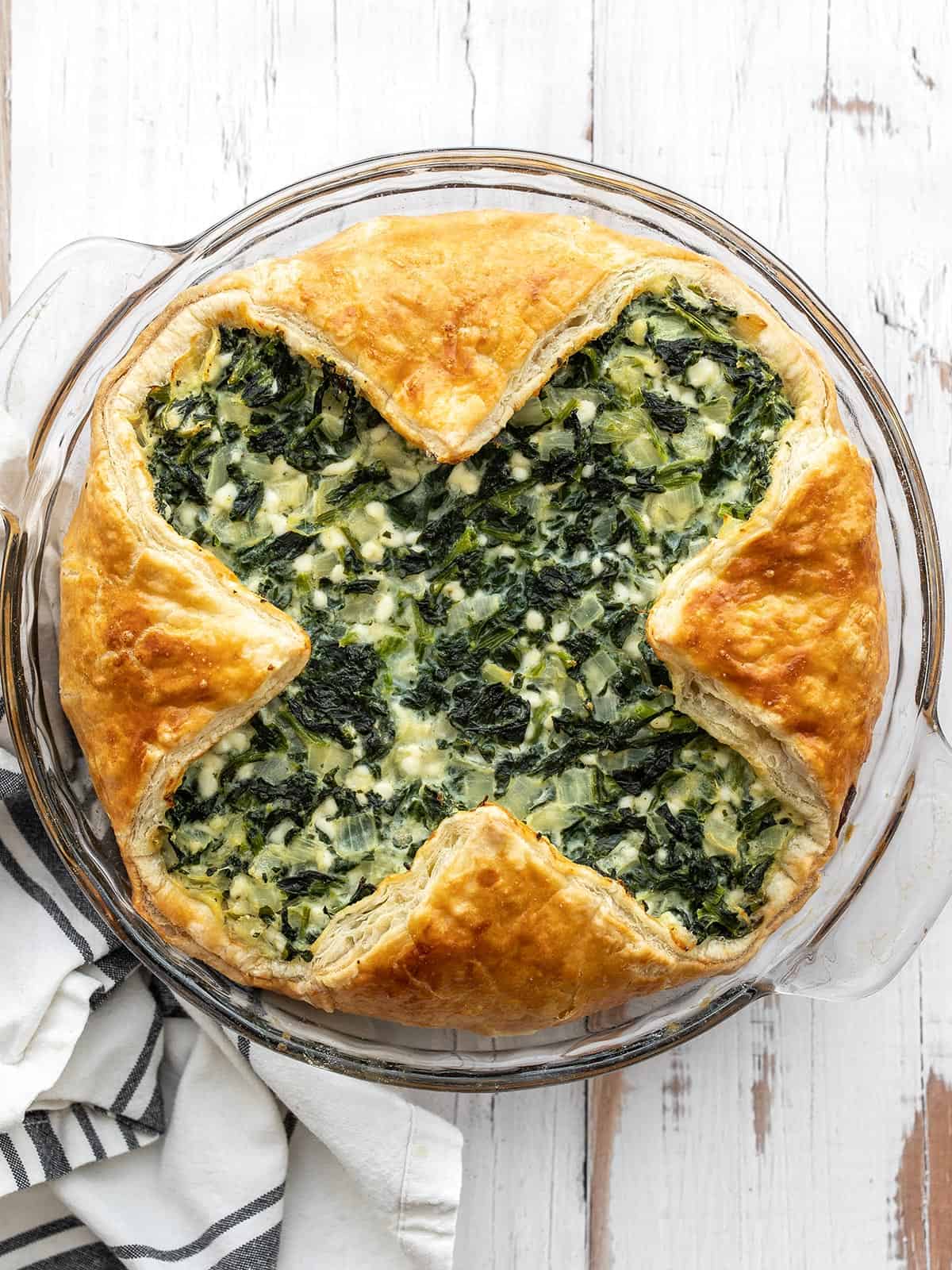 Overhead view of a spinach pie in a glass pie dish on a wood countertop