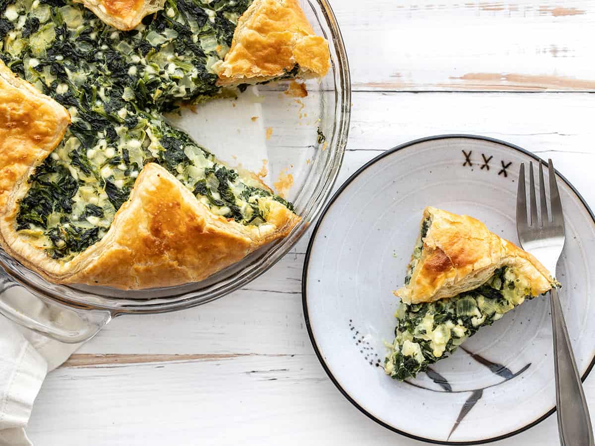 One slice of spinach pie on a plate next to the pie dish
