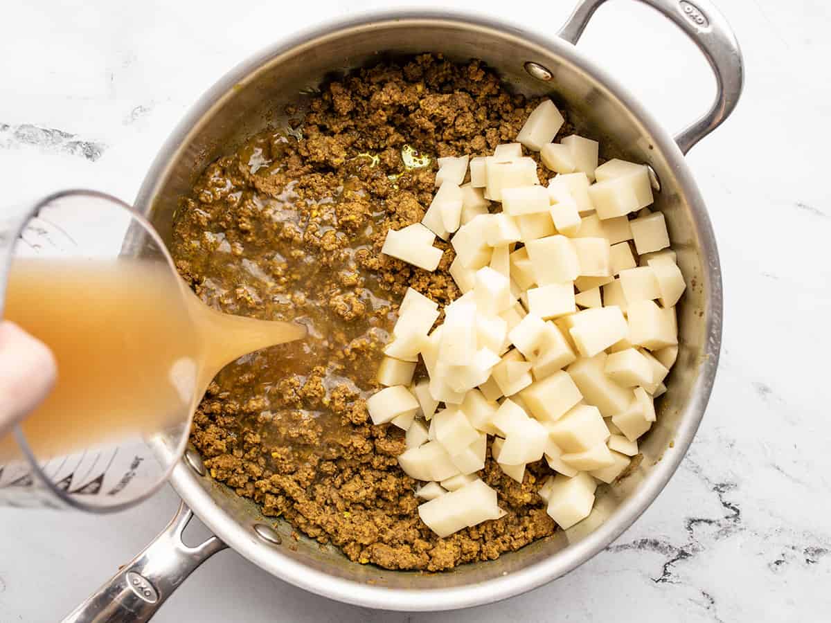 cubed potato in the skillet with beef, broth being poured in the side