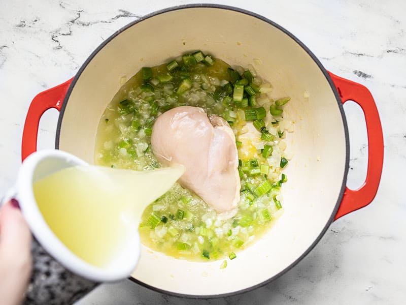 Chicken broth being poured into the soup pot over a chicken breast.