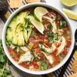 Finished bowl of Chicken and Lime Soup with sliced avocado and a couple of lime wedges