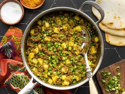curried ground beef with peas and potatoes in a skillet with a serving spoon