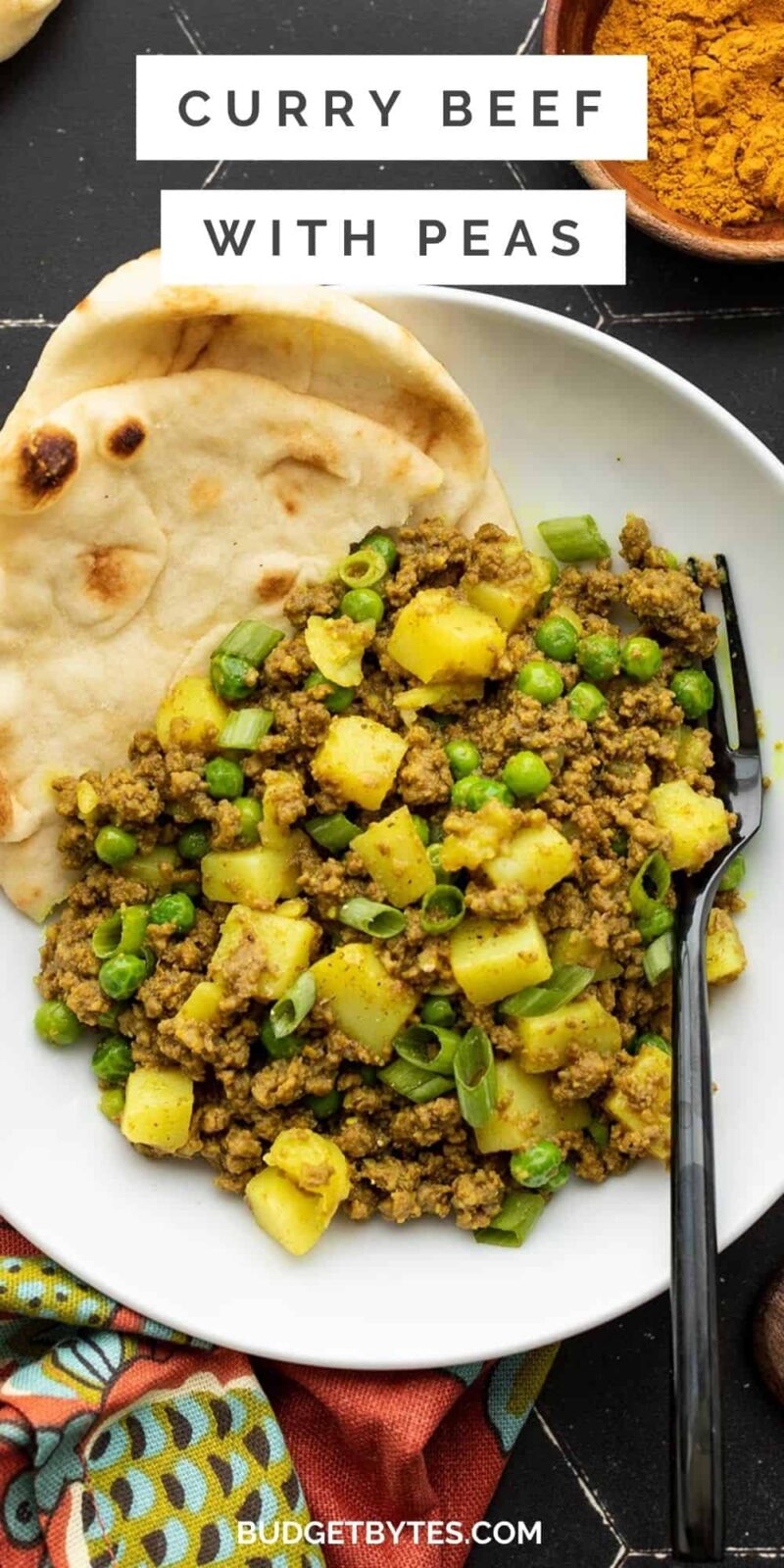 A plate full of curried ground beef with peas and potatoes, naan in the side of the bowl