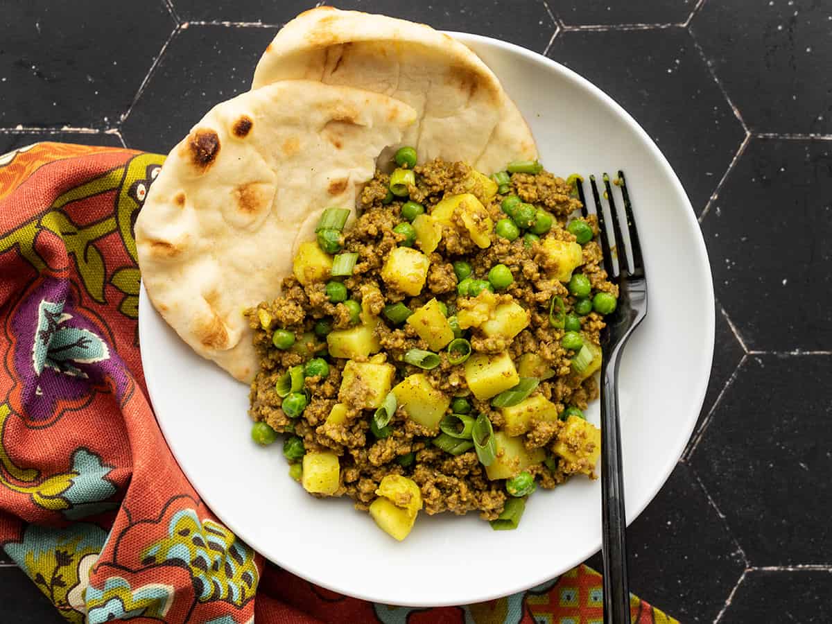 curried ground beef with peas and potatoes in a bowl with naan in the side