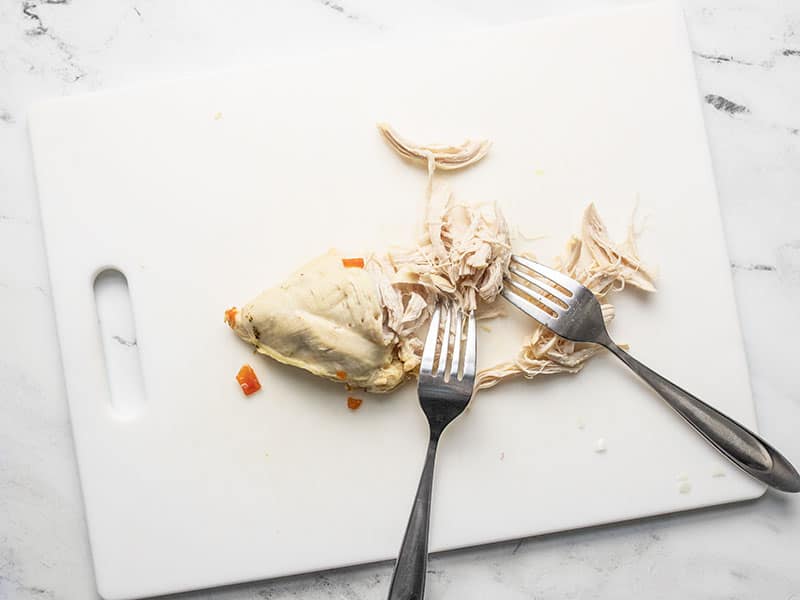 Shred chicken on a cutting board with two knives.