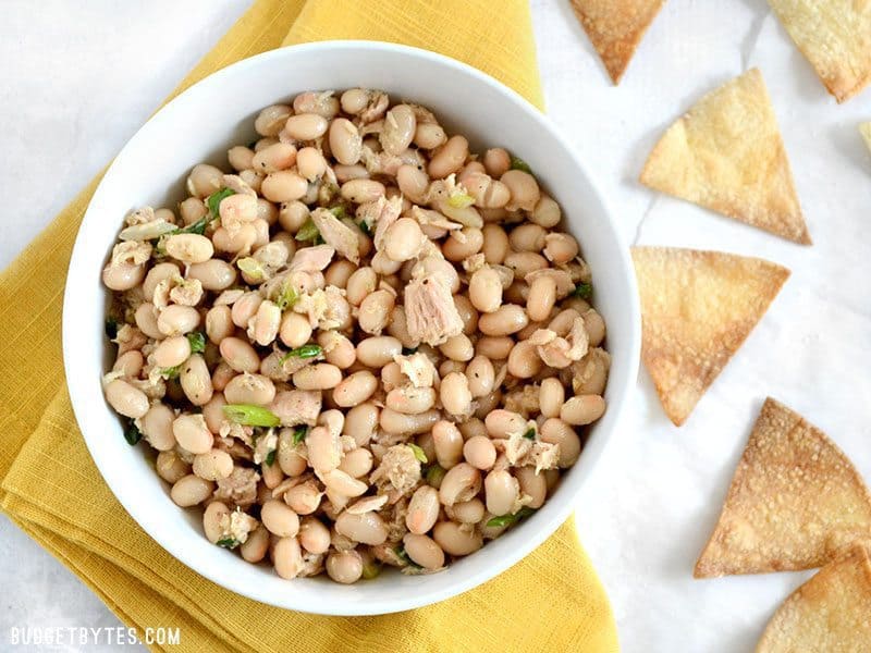 Top view of a bowl of tuna and white bean salad with pita chips on the side 