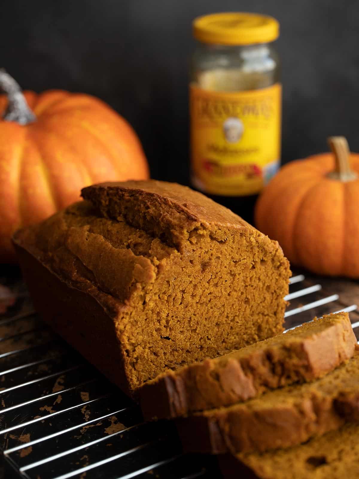 Sliced pumpkin bread on a cooling rack with pumpkins and molasses in the background