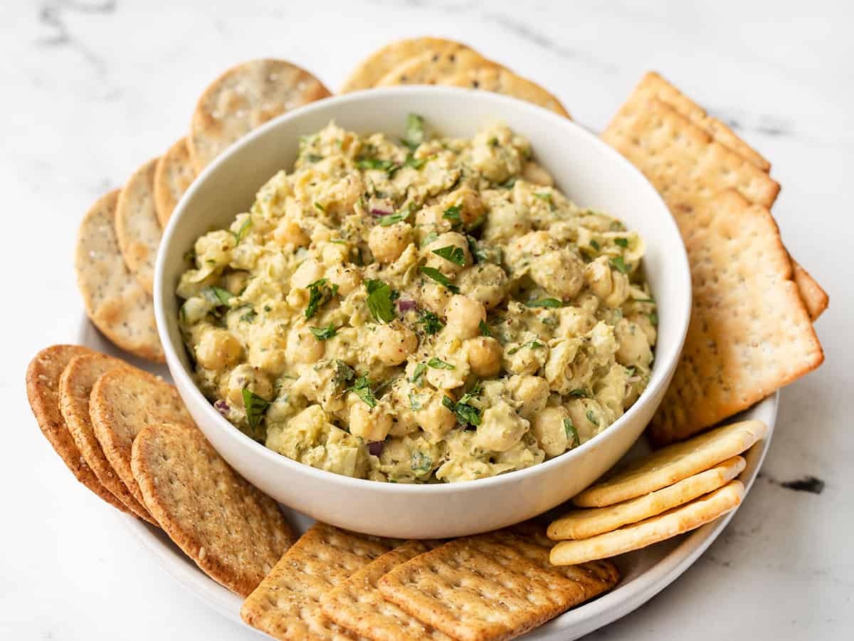 side view of pesto chickpea salad in a bowl, surrounded by crackers