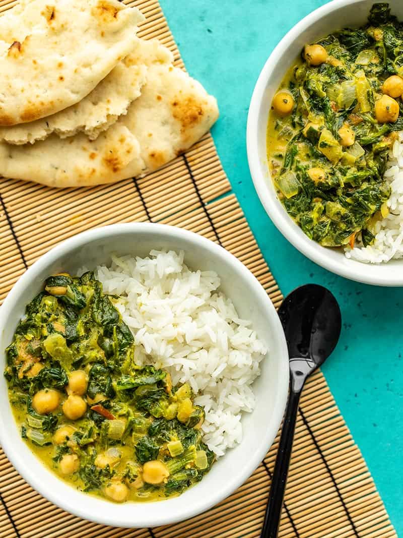 Two bowls of chana saag with rice next to a torn pieces of naan