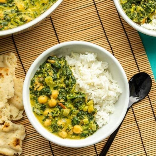 Two bowls of chana saag with rice, next to the skillet and a piece of torn naan