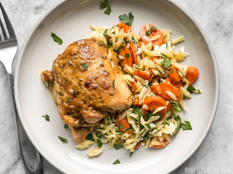 One maple dijon chicken thigh with a side of orzo salad on a plate with a fork on the side 