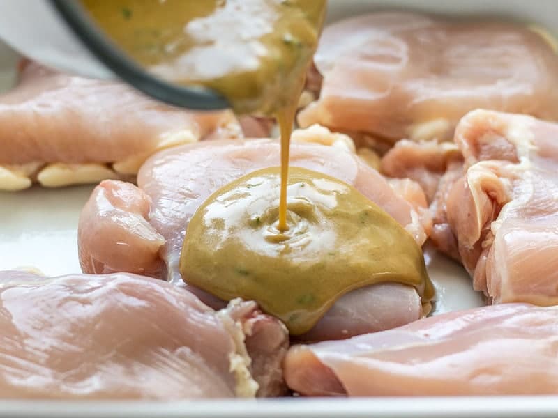 Pouring Maple Dijon Sauce over Chicken in dish 