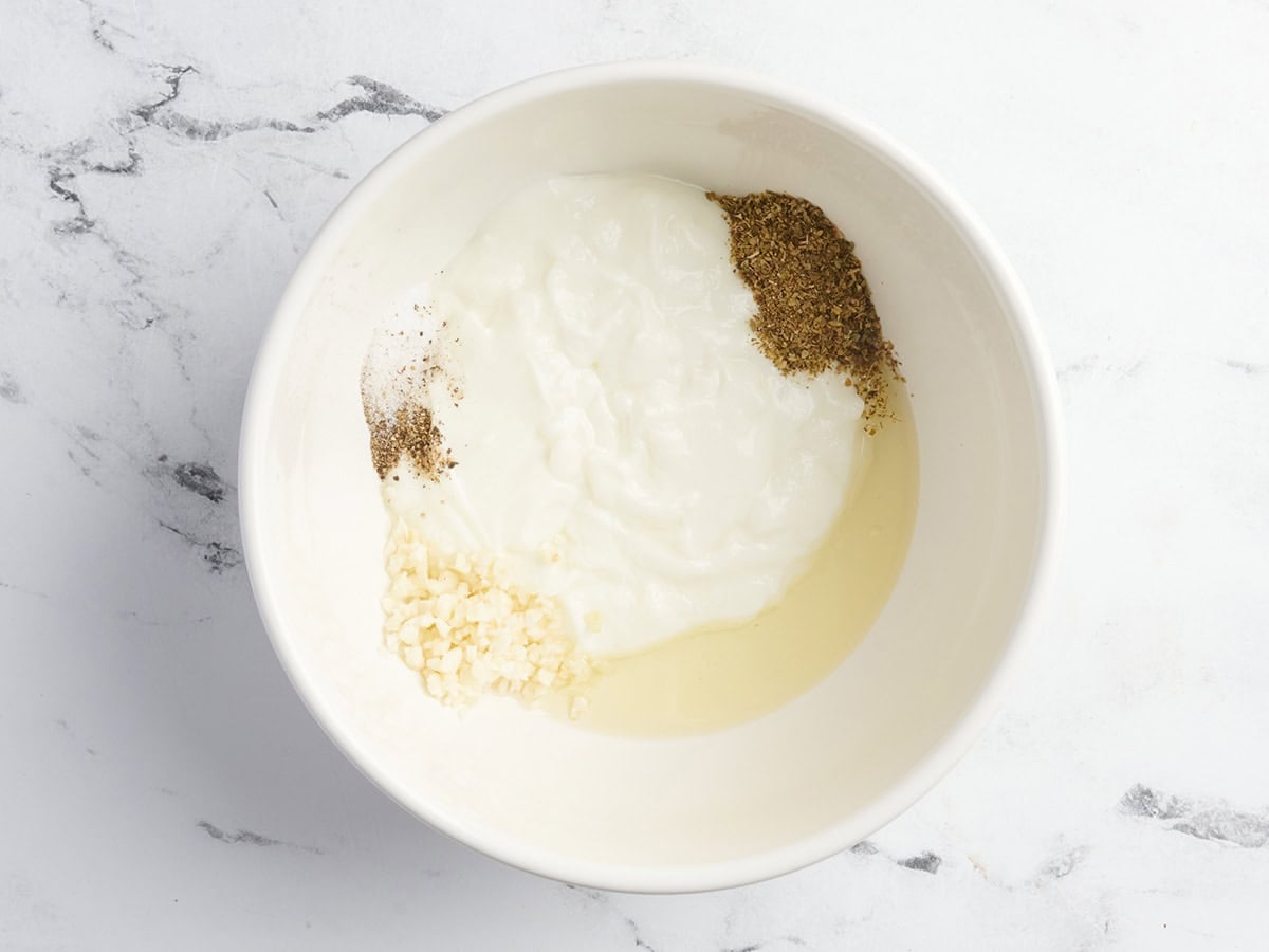 Yogurt, oil, herbs, and garlic in a bowl to make a greek marinade.