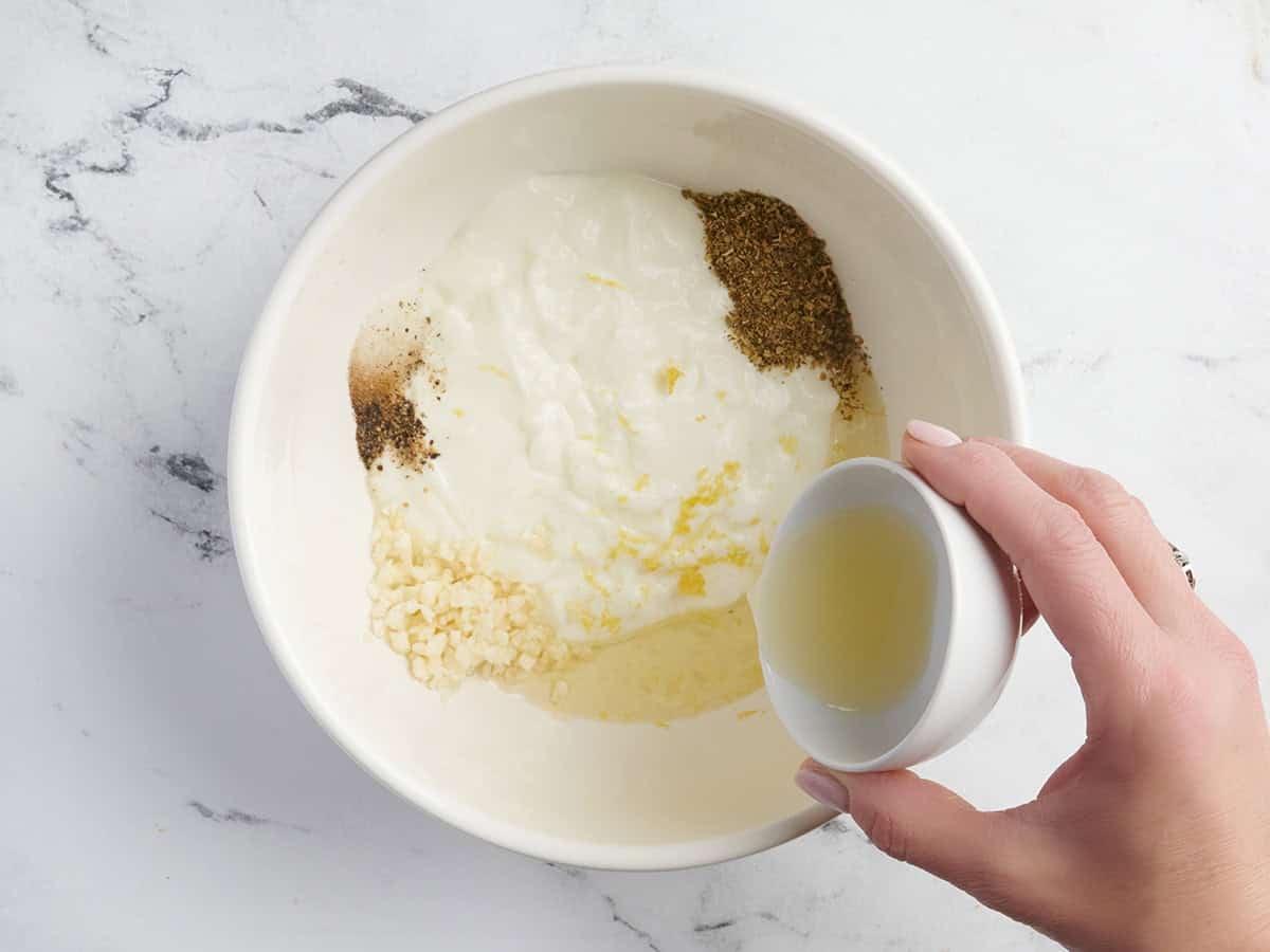 Lemon juice being poured into a bowl of yogurt, garlic and herbs.
