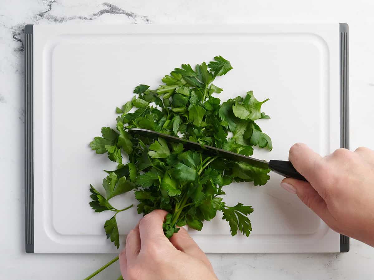 Parsley being chopped on a cutting board.