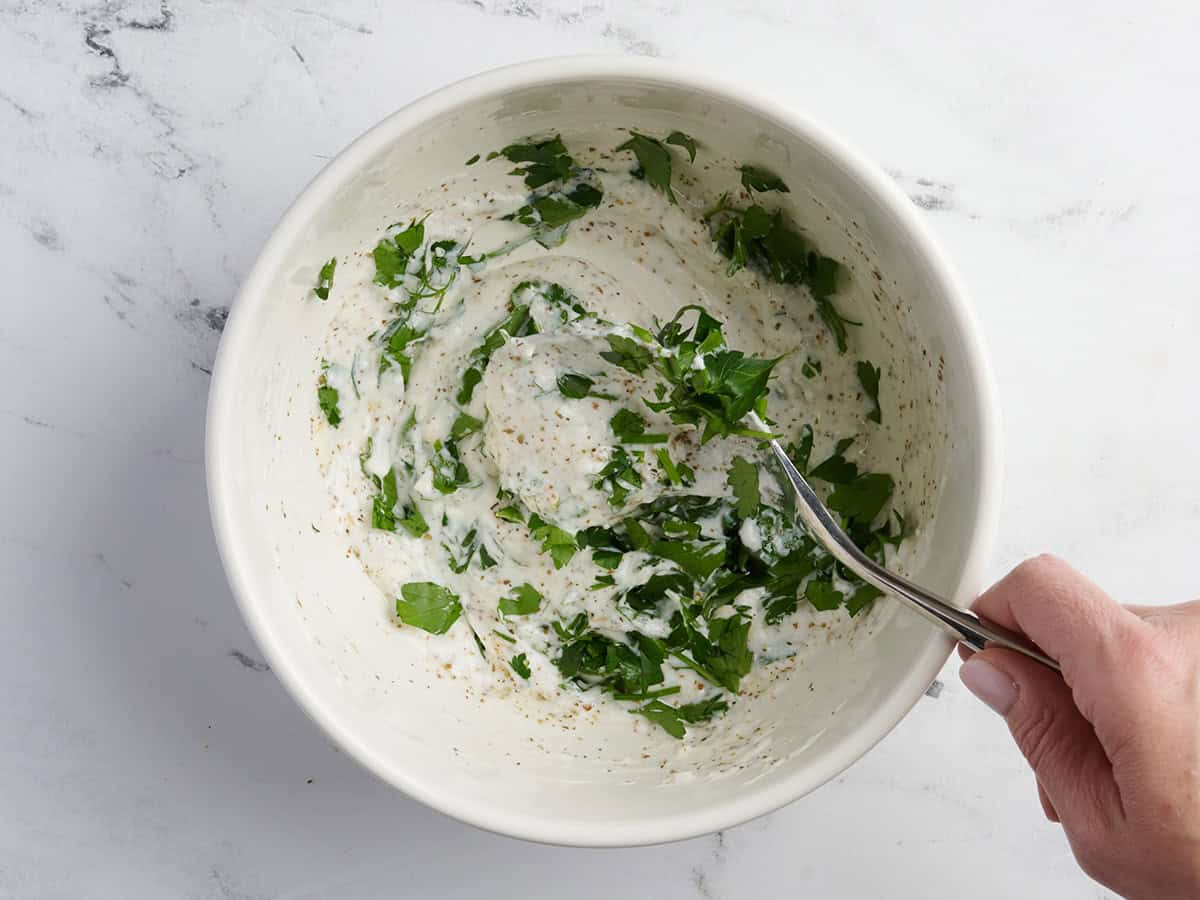 Parsley added to a bowl of greek style chicken marinade.