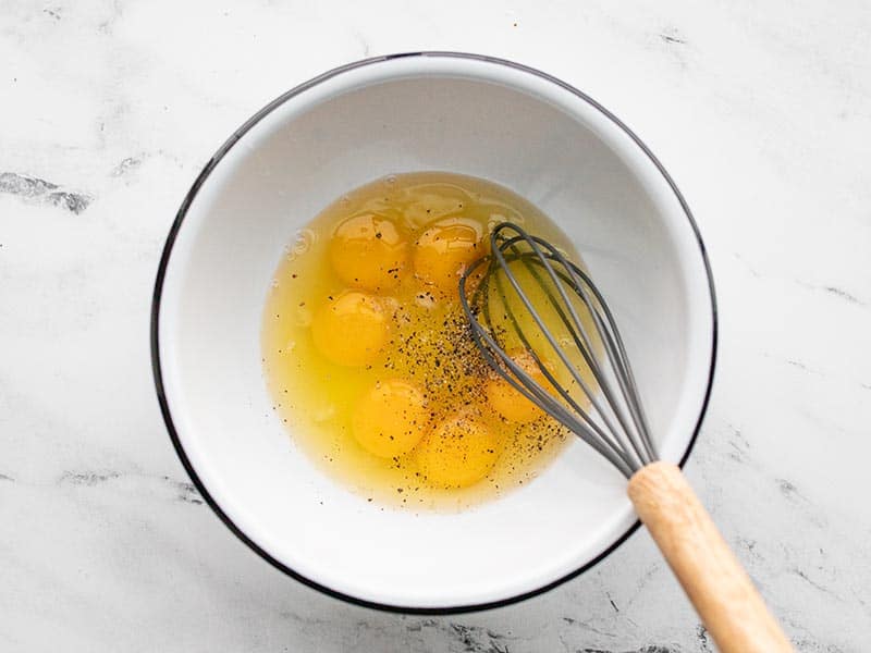 Eggs and a whisk in a white bowl with salt and pepper
