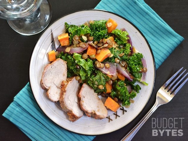 Wilted Kale and Lentil Salad plated on plate with meat and a fork on the side