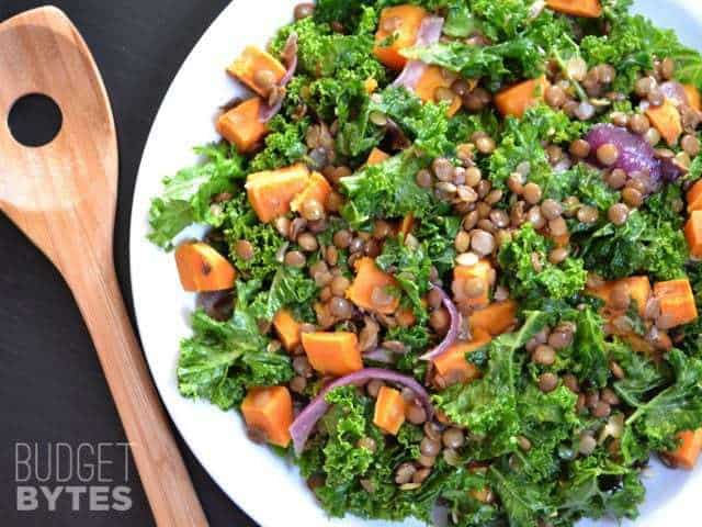Kale Salad Top view of a plate of Wilted Kale and Lentil Salad with a wooden spoon on the side