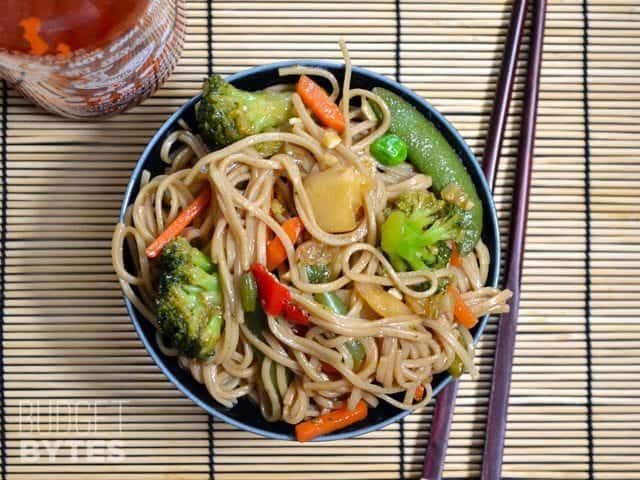 Top view of a bowl of Teriyaki Noodles with chop sticks and a bottle of Siracha on the side 