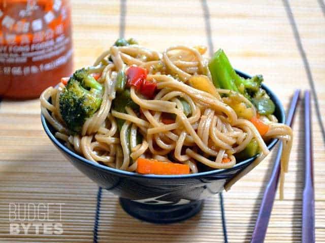 Teriyaki Noodle Bowl with chop sticks and a bottle of Siracha on the side 