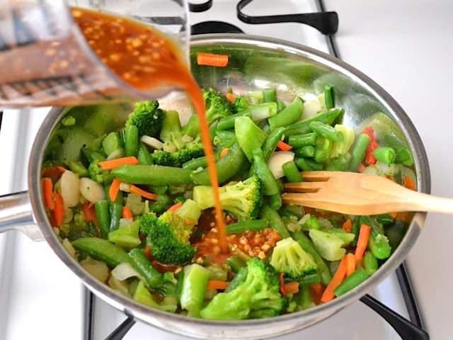 Stir fry Veggies in skillet with sauce being poured over 