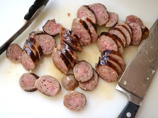 Cooked sausage taken out of pot and sliced with knife 