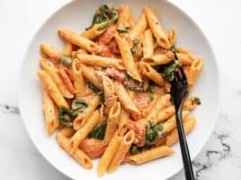 Overhead view of a bowl full of creamy tomato and spinach pasta, a black fork in the side