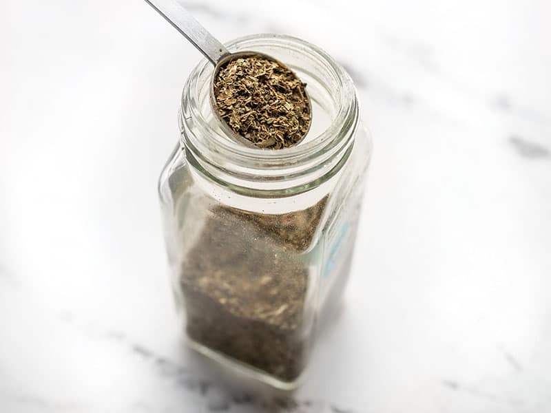 A measuring spoon in a bottle of dried basil