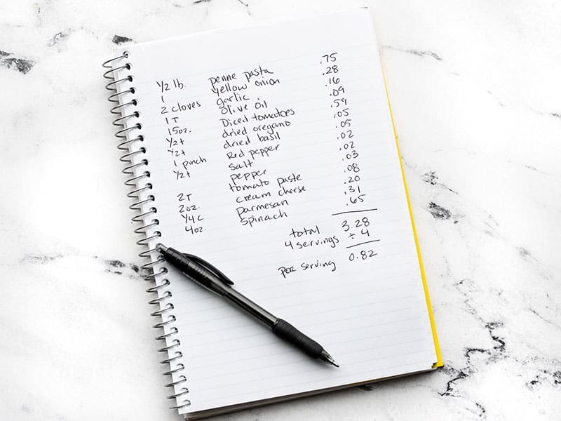 A notebook with a recipe written down and prices listed for each ingredient