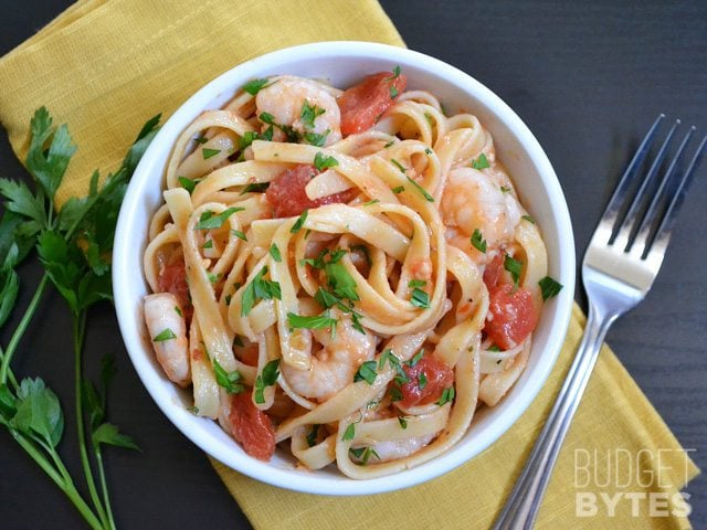 Top view of a bowl of spicy shrimp tomato pasta with fork on the side 