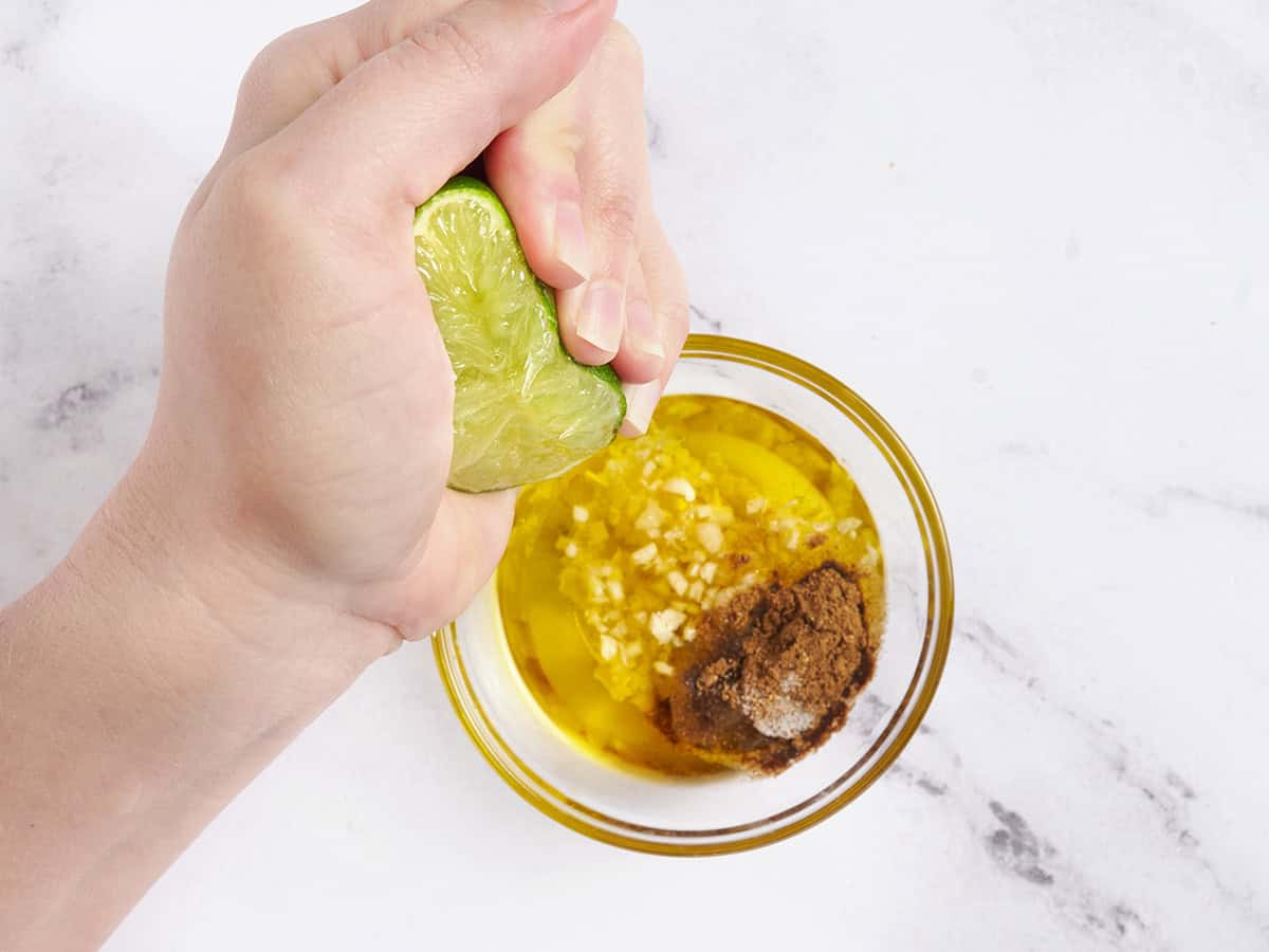 A hand squeezing a lime into a steak marinade.