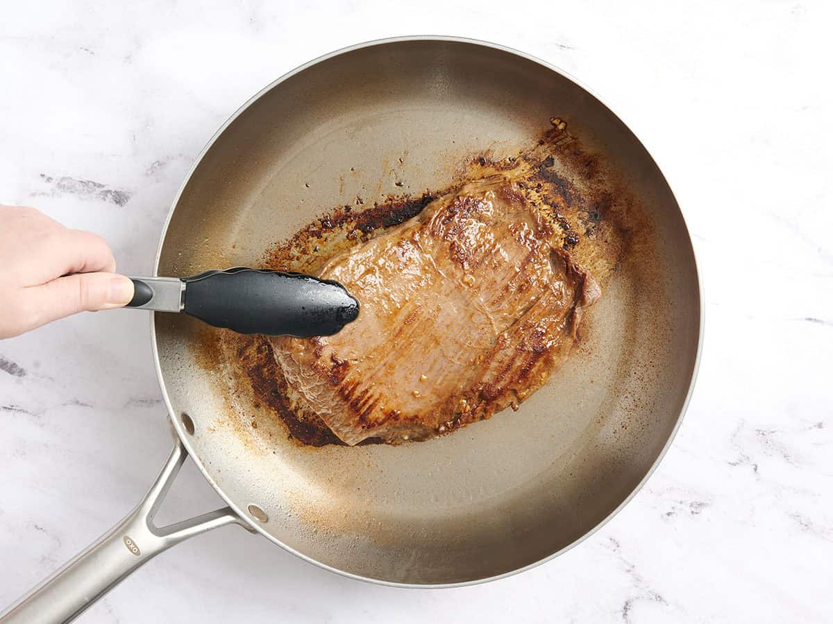 A flank steak cooking in a skillet.