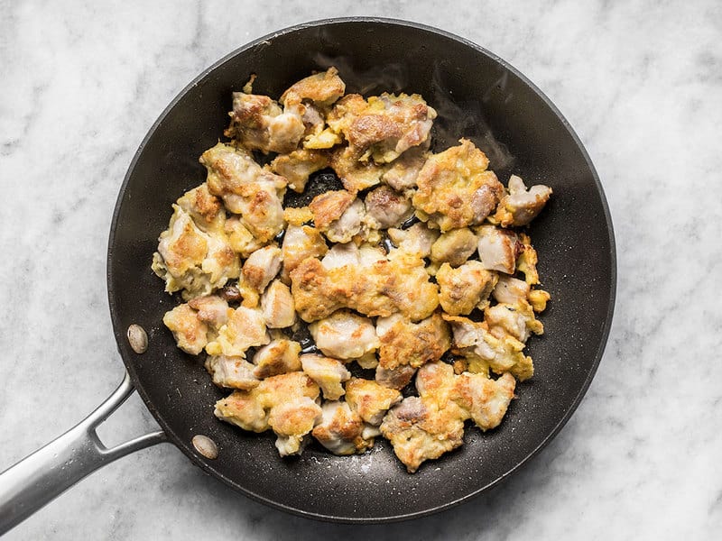 cooked chicken in skillet with light egg and cornstarch coating.