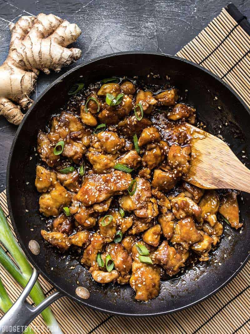 This incredibly Easy Sesame Chicken is faster and tastier than take out. You control the ingredients, you control the flavor. Budgetbytes.com A skillet full of easy sesame chicken with a wooden spatula on a bamboo mat.