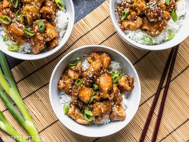 Three bowls of easy sesame chicken with rice on a bamboo mat