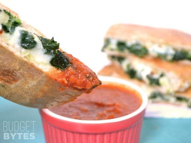 Close up of a half of a Spinach Feta Grilled Cheese being dipped into marinara sauce 