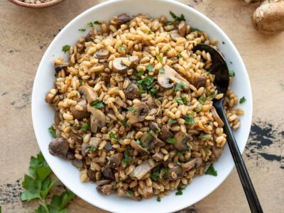 overhead view of baked barley with mushrooms in a serving bowl with a spoon