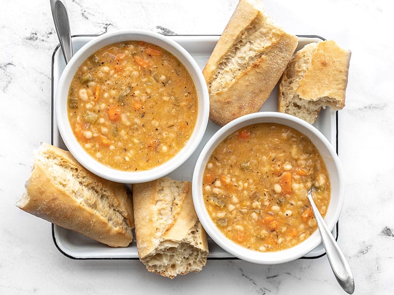 Overhead view of two bowls of slow cooker white bean soup with pieces of baguette on the sides