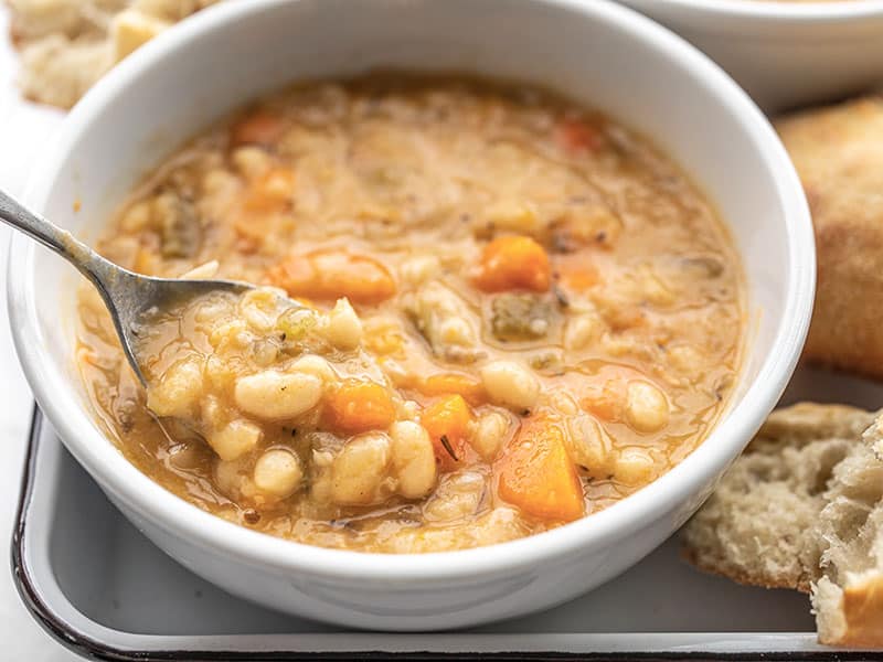 Close up of a spoon lifting a bite of slow cooker white bean soup out of a bowl