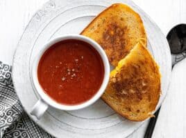 Tomato herb soup in a mug on a plate with grilled cheese