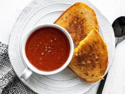 Tomato herb soup in a mug on a plate with grilled cheese