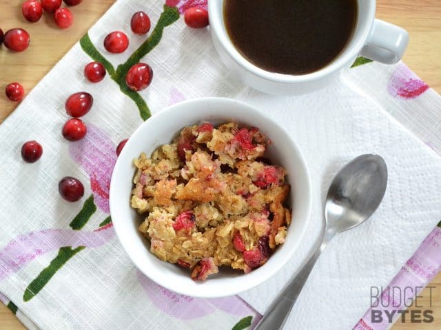 Top view of a bowl of Cranberry Apple Baked Oatmeal with a cup of coffee in background and spoon on the side 